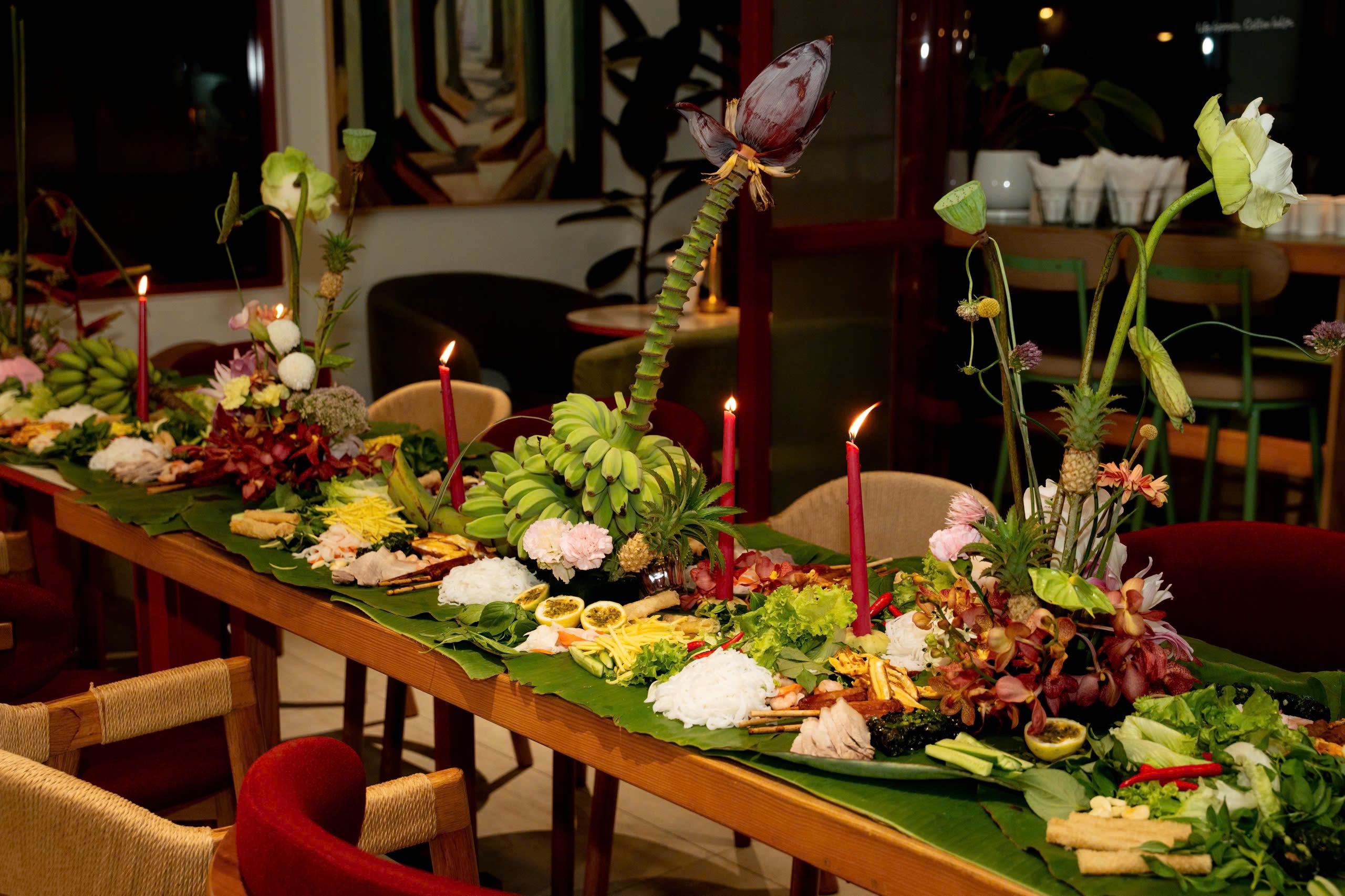 Long banana leaf table runner with green bananas, banana blossom and red candles